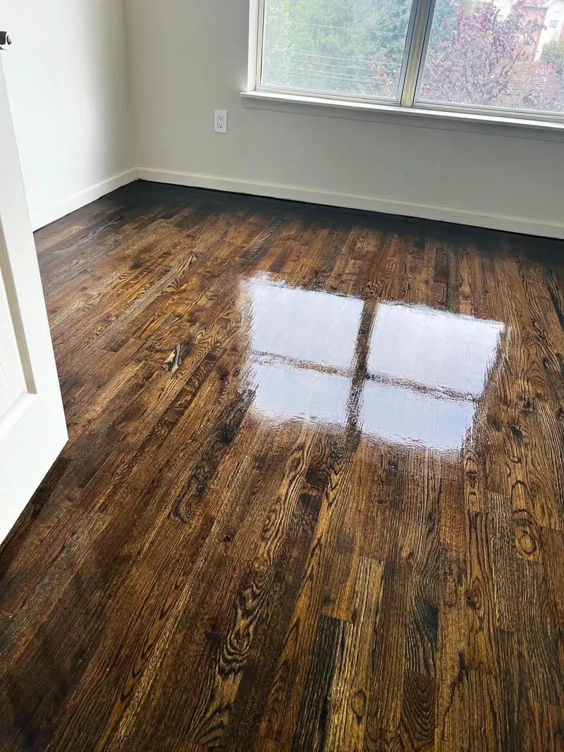 Hardwood floor refinished with a dark stain and glossy topcoat reflecting window light